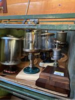 Collection of vintage glass oilers with metal lids and valves, mounted on wood bases inside a green metal box.