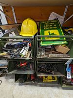 View showing the yellow hard hat, John Deere sign, and bins with various vintage hand tools and hardware items such as washers and screws.