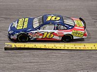 Side view of the 2006 Greg Biffle Ford Fusion NASCAR diecast car with National Guard decals and number 16 on roof and doors, placed on a wood surface with measuring tape showing approximately 8 inches in length.