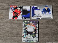 Three NHL jersey cards arranged on wooden surface: Nicklas Lidstrom Hall of Fame Legends, Ilya Mikheyev Young Guns Rookies, Isaac Ratcliffe Rookies.
