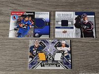 Front side of three NHL jersey trading cards laid out on wooden surface showing player images and jersey swatches.