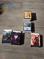 Four deck boxes for Magic: The Gathering cards with distinctive fantasy character artwork placed on a wooden surface