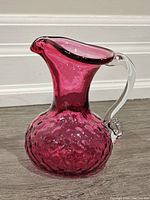Front view of cranberry art glass jug with clear handle, showing textured body and flared spout