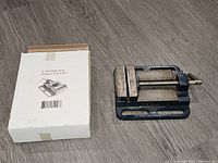 Photo of the 4 inch drill press vice beside its original box showing the complete item and packaging.