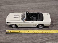 Side view of white 1969 Camaro SS die cast model car with convertible roof down, showing the full length and detailing of the car against a wooden floor background, with a measuring tape indicating about 10 inches length.
