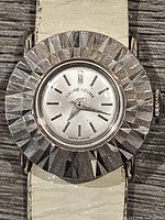 Close-up photo of Favre Leuba watch face showing silver-tone textured bezel, white dial, and silver baton markers and hands.