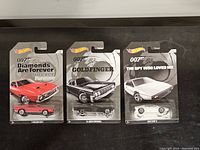 Photo shows all three Hot Wheels cars in original packaging: Red '71 Mustang Mach I, black '64 Lincoln Continental, white Lotus Esprit S1.