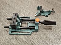 Large metal tool maker's vice showing base, jaws, screw mechanism, and handle in teal-green and black.