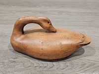 Side profile of wooden duck decoy showing curved neck and natural wood finish with speckled markings.