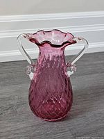 Front view of cranberry art glass vase showing diamond pattern and clear glass handles with scalloped rim.