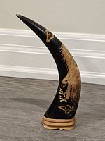 Front view showing bird head and claws carved into the curved water buffalo horn mounted on a wooden base.
