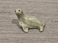 Front left side view of the seal figurine on a wood surface showing its shape and polished green soapstone.