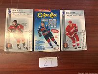 Photo showing three unopened boxes of hockey cards on a wooden surface with a paper labeled '27'.