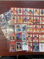 Photo showing multiple baseball cards laid out on a wooden table; features player portraits and some cards in plastic sleeves; includes cards from the Topps series and "The Griffey's" series.