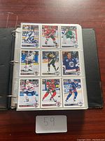 Photo of an open binder page with nine hockey cards in plastic sleeves featuring various NHL team uniforms and players.