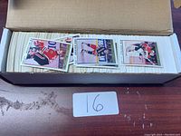 Open cardboard box filled with an assortment of loose hockey cards with a few cards fanned on top showing players in uniform.