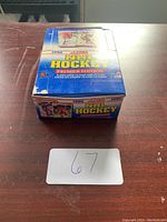 Closed blue and white box labeled '1990 Score NHL Hockey Premier Edition' on a wooden surface. Seller lot number 67 visible.
