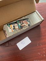 Photo showing an open cardboard box packed with a large number of hockey trading cards. Some cards are loose at the top showing players in hockey gear.