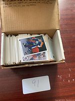 Open cardboard box filled with a large number of hockey trading cards, some facing up revealing player images in jerseys.