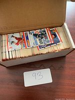 Open box filled with hockey cards in protective sleeves showing a few cards on top with players in various team uniforms.