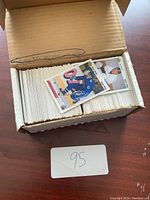 Photo showing a cardboard box filled with many hockey cards, some individual cards visible on top, sleeved for protection.