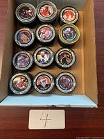 Photo shows the top of approximately a dozen hockey coins arranged in a box, each with a colored image of a hockey player in uniform and team/league information around the edge.