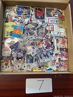 Single cardboard box containing mixed loose hockey trading cards and stickers, visible sealed NHL sticker pack and numerous loose cards and stickers.