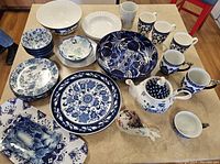 Overview of all items in the lot showing dinner plates, bowls, mugs, teapot, and decorative bird on a table.
