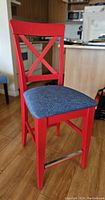 Front angled view of counter height chair showing red painted wooden frame, X-back design, and blue padded seat.