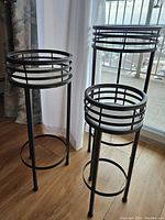 Overall view of the three black metal plant stands showing the differences in height and cage-like round top design.