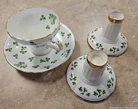 Set of shamrock-themed tea cup, saucer, and two candle holders, showing detail of design and gold trim.