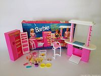 Full view of the Barbie Kitchen Playset including refrigerator, kitchen counter with stove, chair, and various accessories, along with original box in background.
