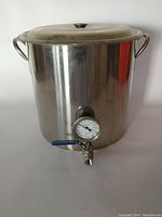 Front view of the large stainless steel brew kettle with handles and lid showing ball valve and thermometer.