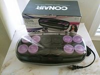 Set of 12 ceramic oversized hot rollers seated in black heated base with clear cover, power cord and box in background