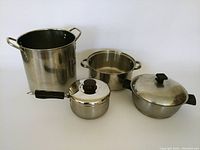 Four cooking pots and pans shown together, including a tall stock pot without lid, a medium pot without lid, a small Lagostina pot with lid, and a Rena pot with lid and plastic handles.