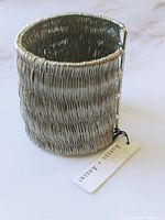 Close-up image of wide silver bangle showing textured wire woven design and Aureus + Argent brand tag.