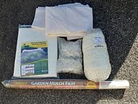 Complete set of garden mulch film, frost protection fabric, white plastic clips, and protective netting trellis laid out on black surface.