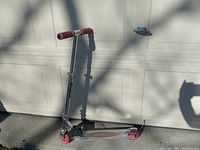 Full view of the silver Razor scooter with pink handlebars and wheels against a white garage door. Shows the handlebars with wear and overall structure.