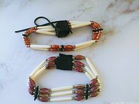 Top view of two handmade First Nations chokers placed side by side showing bone beads, decorative purple and orange beads, with black leather ties and accents.