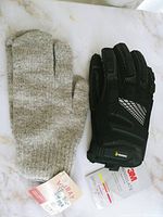Photo showing beige 100% wool ladies mitts and black working gloves with tags on a marble surface.