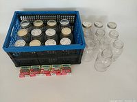 Full lot displayed: multiple used canning jars with metal lids both attached and detached, arranged in a plastic crate and alongside it. Five unopened boxes of Bernardin snap lids placed in front.