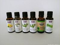 Photo showing six amber glass essential oil bottles with black caps and labels for lemon, lemon eucalyptus, white thyme, sweet basil, and lemongrass oils from NOW Essential Oils and Penny Lane Organics.