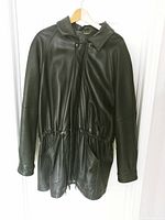Black Danier men's leather coat hanging on a wooden hanger, front view with zipper covered by snap button flap, cinched waist with drawstring visible.