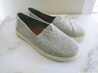 Side angle view of light gray canvas TOMS shoes showing slip-on style and rubber sole.