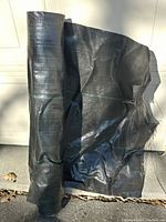 View of black woven landscape fabric partially unrolled, showing texture and green weave lines.