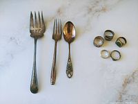 Photo showing 2 Birks sterling silver utensils (spoon and serving fork), 1 Wallace sterling silver fork, and 5 sterling silver rings.