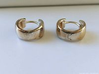 Close-up side view of both sterling silver huggie earrings showing the hinged design and polished surface with some tarnishing.