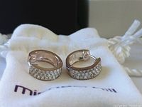 Pair of sterling silver reversible huggie earrings with one side set with small sparkling stones, placed on a white soft pouch branded 'michael hill'