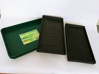 Photo shows one green garden tray with a garden tray label alongside two black shallow trays with ribbed bottoms.
