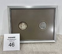 Front view showing two 1983 Canadian silver dollars mounted in a silver frame with beige background.